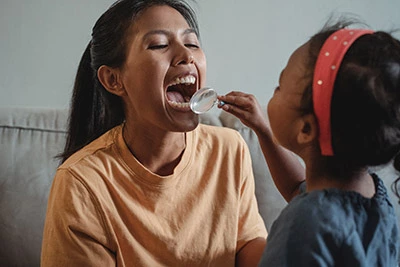 child doing a pretend dental checkup on her mom